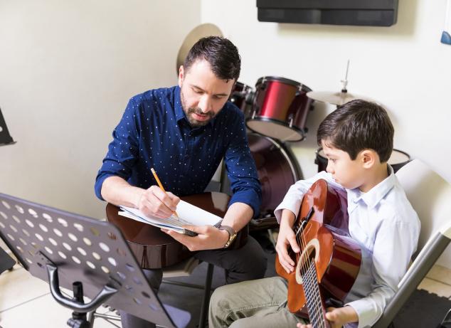 Student learning guitar lessons with instructor.